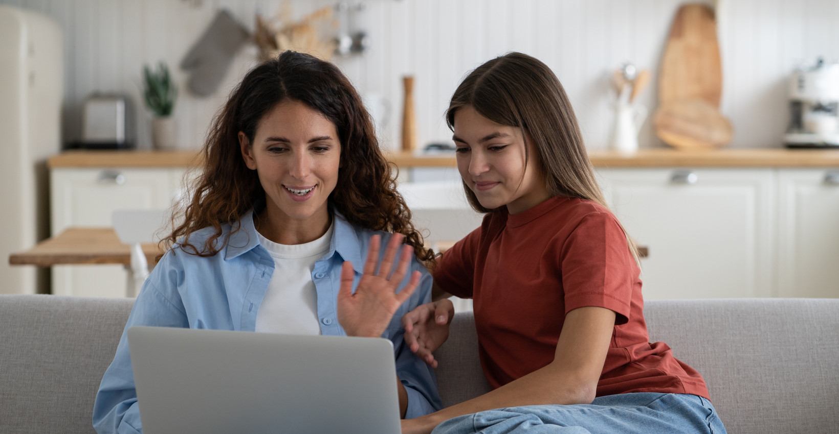 a mother and daughter sit on a couch looking at a computer together