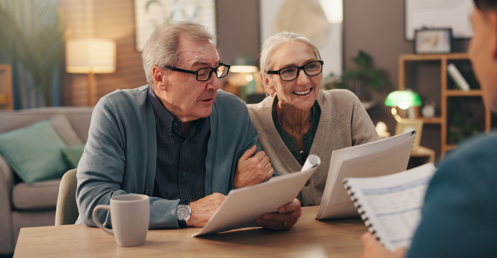an elderly couple sits at a table reviewing paperwork