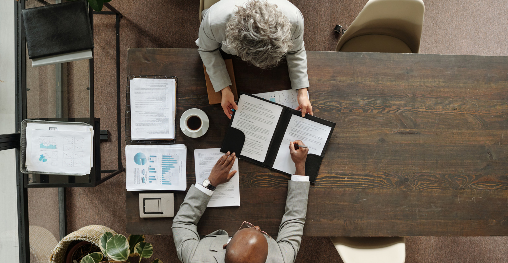 An overhead angle of two people having a meeting at a wooden table
