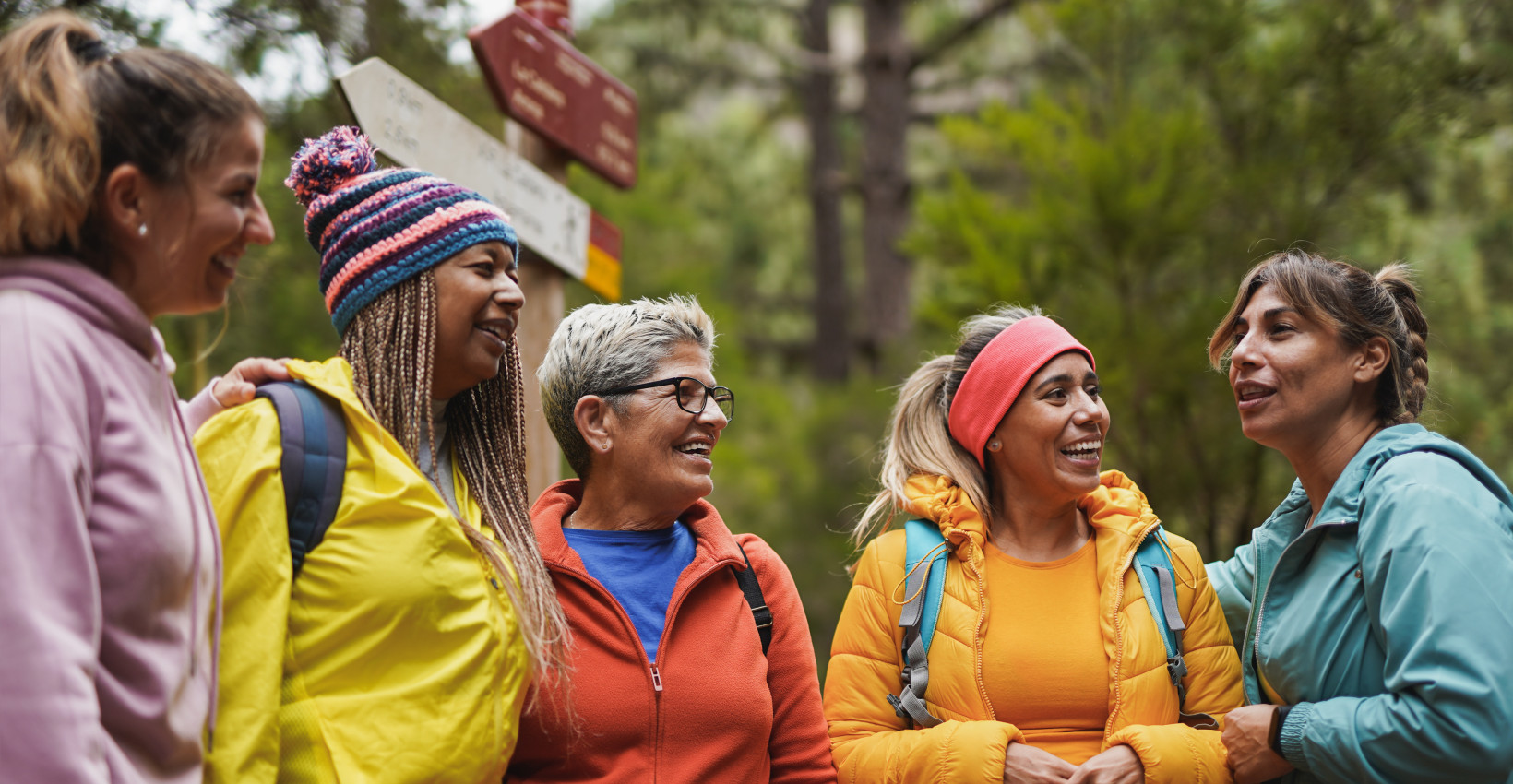 a group of women stand together outside in hiking gear laughing