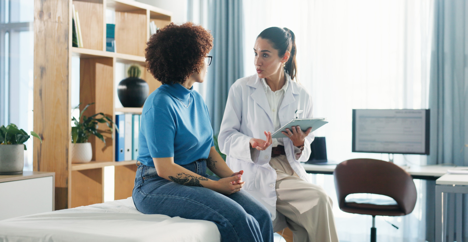 a female doctor sits with a female patient in an exam room