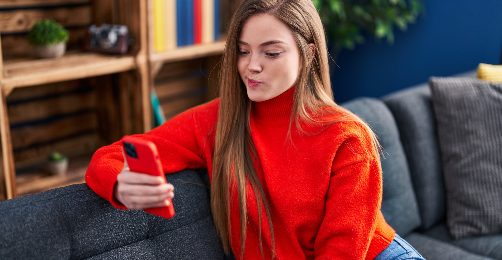 a woman sits on her couch holding her phone