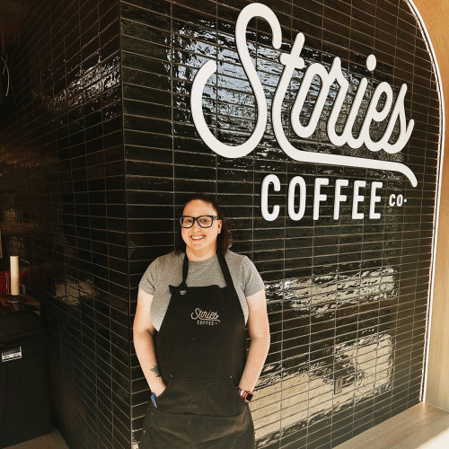 A man stands in front of a wall that says "Stories Coffee"