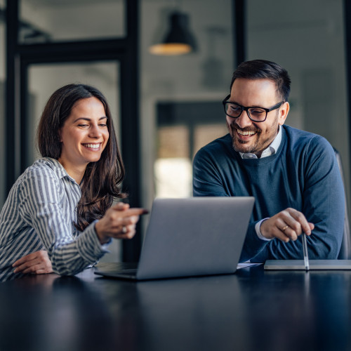 two people smiling as they work on a laptop