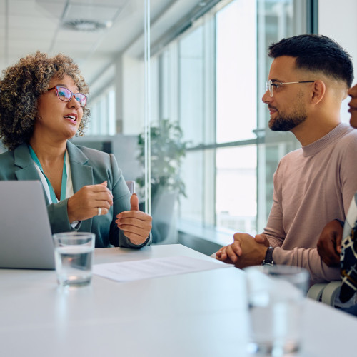 A woman in a suit talks to a couple sitting at a table about finances