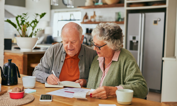 an elderly couple sits together at a table reviewing documents