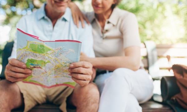 an older couple looks at a map while sitting on a park bench