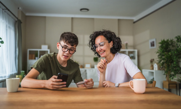 a mom and son sit at a table looking at a phone together