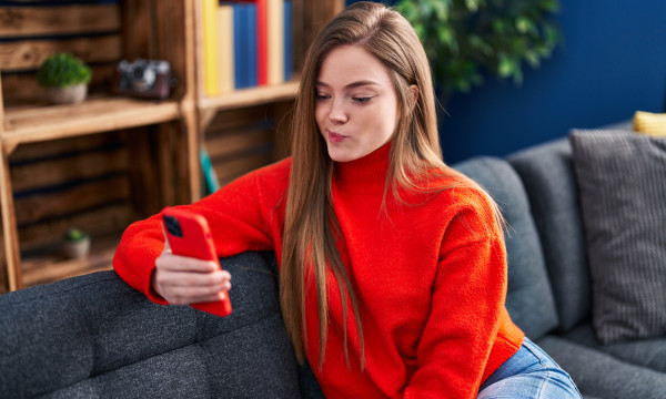 a woman sits on her couch holding her phone